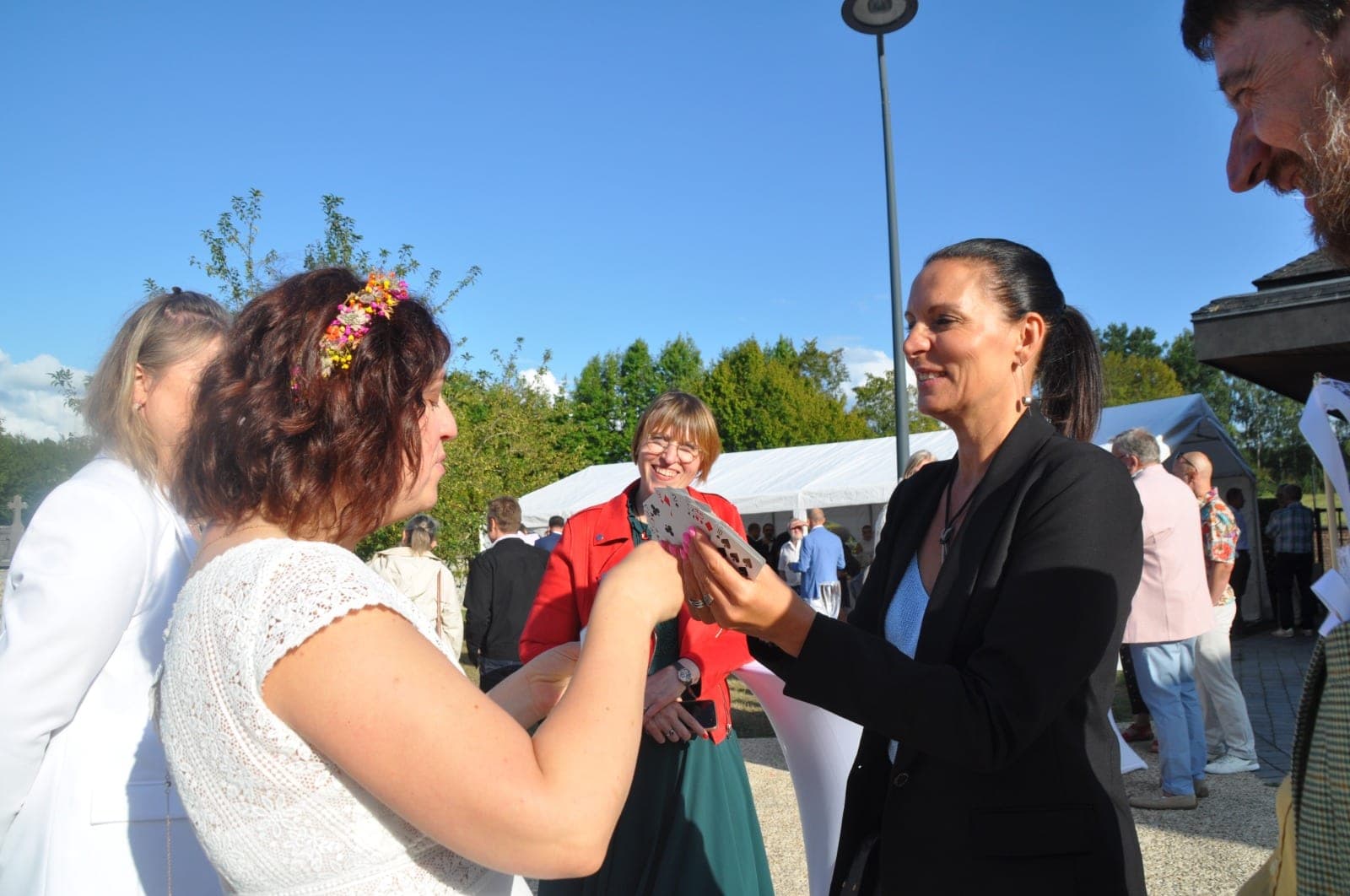 Karine présente un éventail de cartes à la mariée, qui en choisit une, sous un ciel bleu